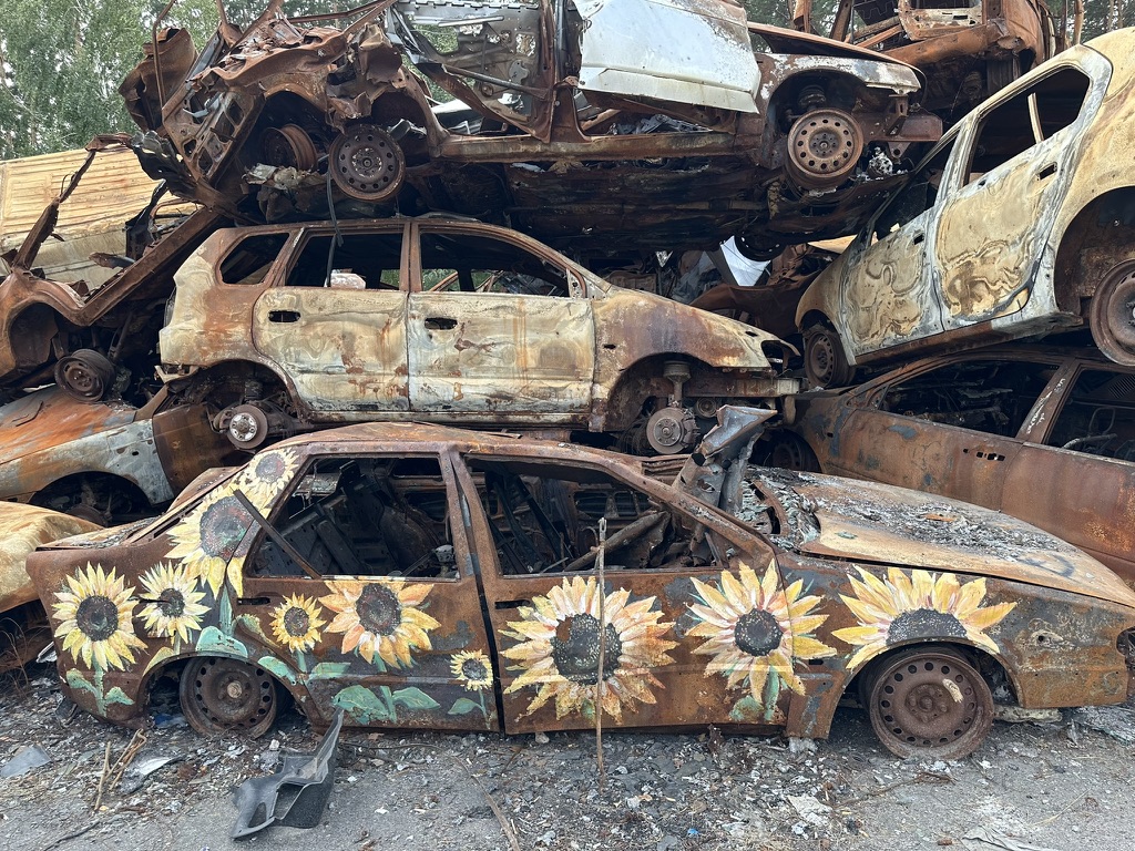 Pile of destroyed, rusted cars, one painted with sunflowers