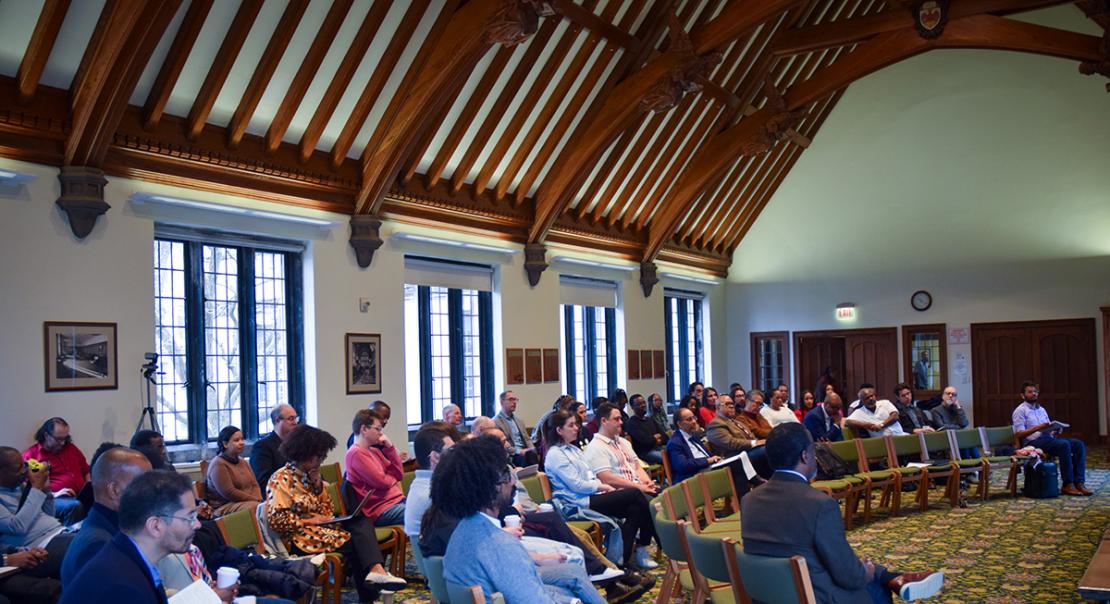 Symposium audience seated in a semi-circle listening and writing notes.